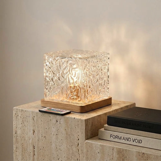 AURA Cube on a wooden desk, amber light and liquid reflections on the wall behind
